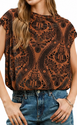 Woman wearing a brown patterned top and blue jeans on a white background