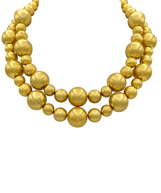 A gold beaded statement necklace with multiple strands of matte and textured spherical beads, photographed against a solid white background.